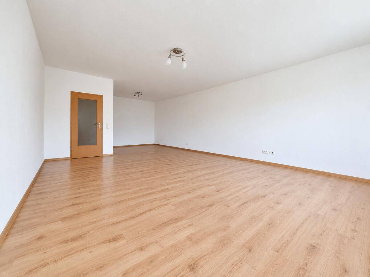 Leeres, geräumiges Wohnzimmer mit Laminatboden und weiß gestrichenen Wänden.