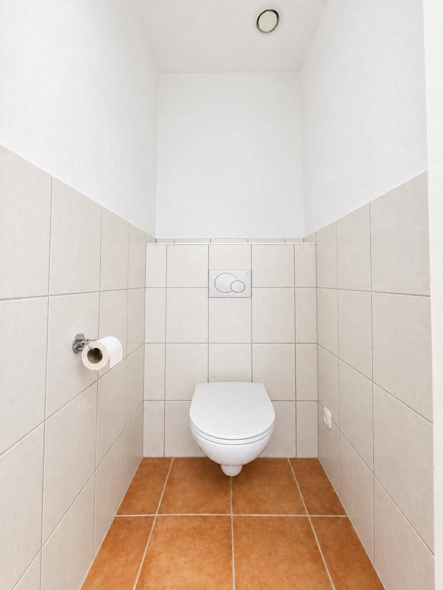 Separates WC mit Wand-WC und hellen Fliesen an Wänden und Boden.
