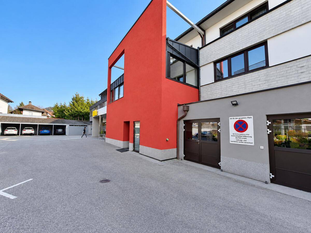 Moderne Gebäudefassade mit rotem Akzent und Außenparkplätzen.