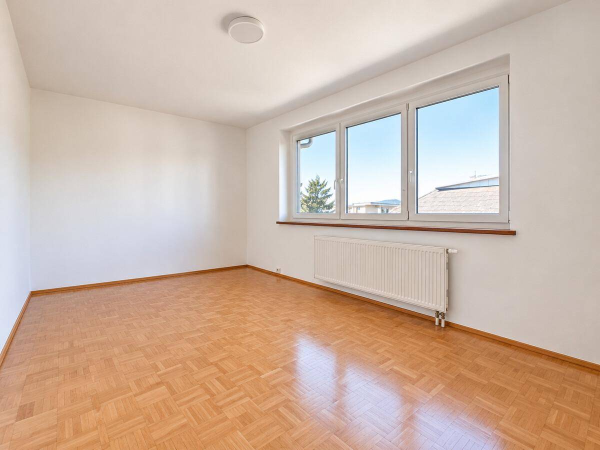 Helles Schlafzimmer mit Parkettboden, großen Fenstern und Blick auf die Umgebung.
