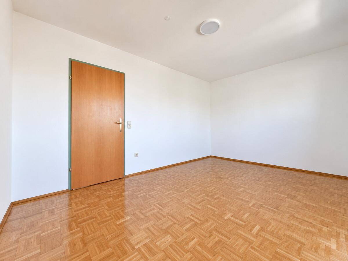 Leeres Zimmer mit Parkettboden und Holztür, bereit zur individuellen Gestaltung.