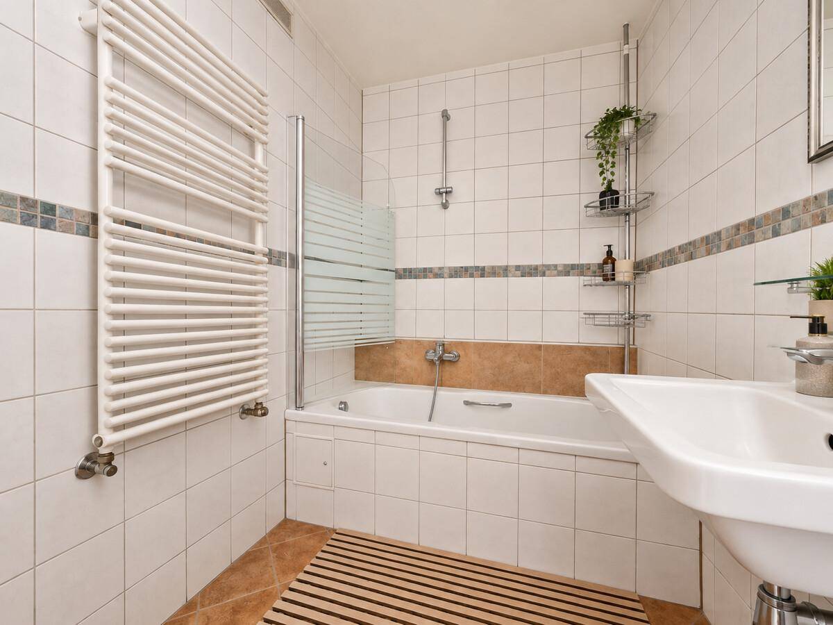 Gefliestes Badezimmer mit Badewanne, Duschabtrennung und beheiztem Handtuchhalter.