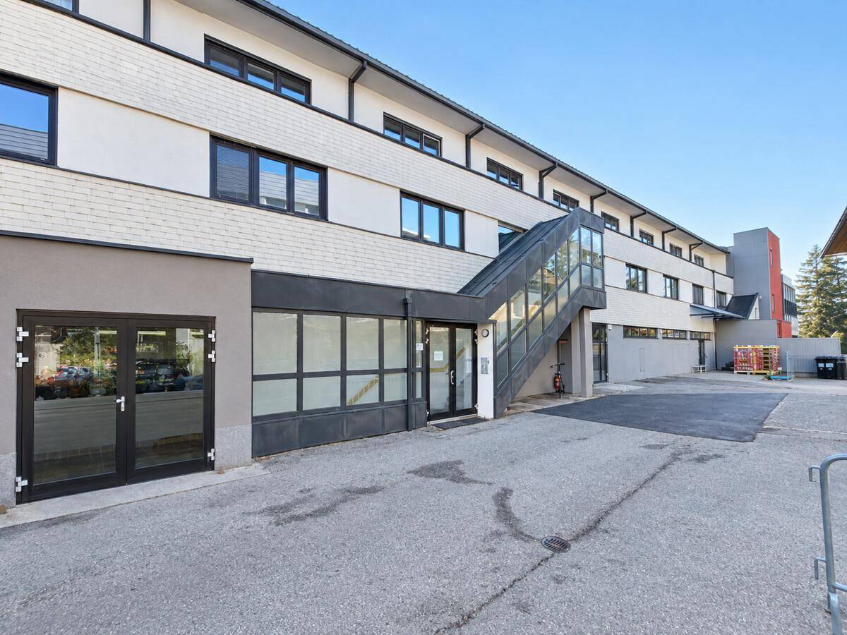 Moderne Gebäudefassade mit mehreren Etagen, externer Treppe und gepflastertem Vorplatz.