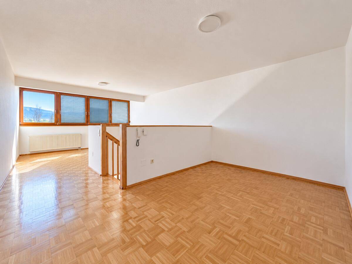 Offener Raum im Obergeschoss mit Parkettboden, Galerie und großen Fenstern.