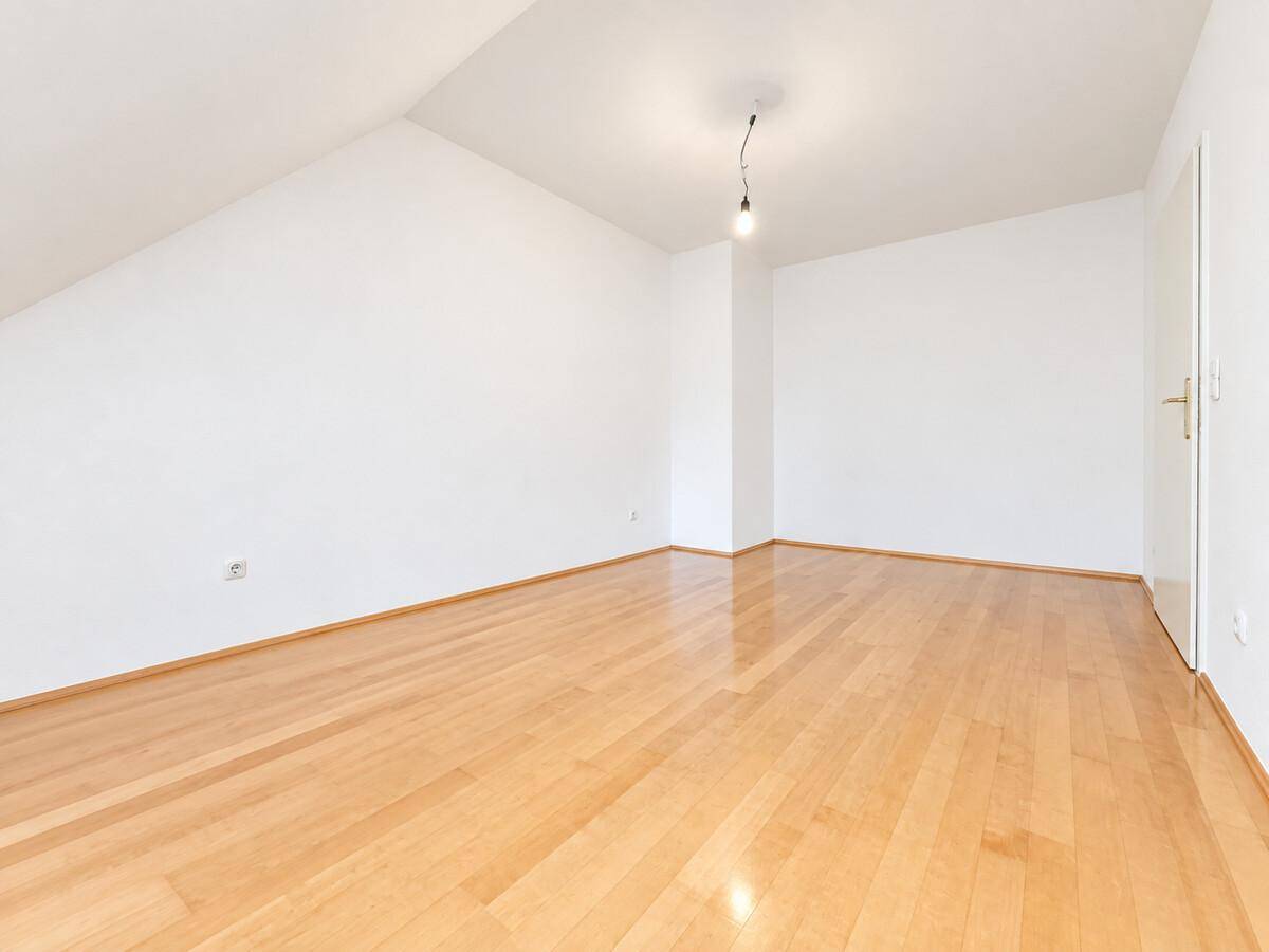 Helles, leeres Dachgeschosszimmer mit Parkettboden und weiß gestrichenen Wänden.