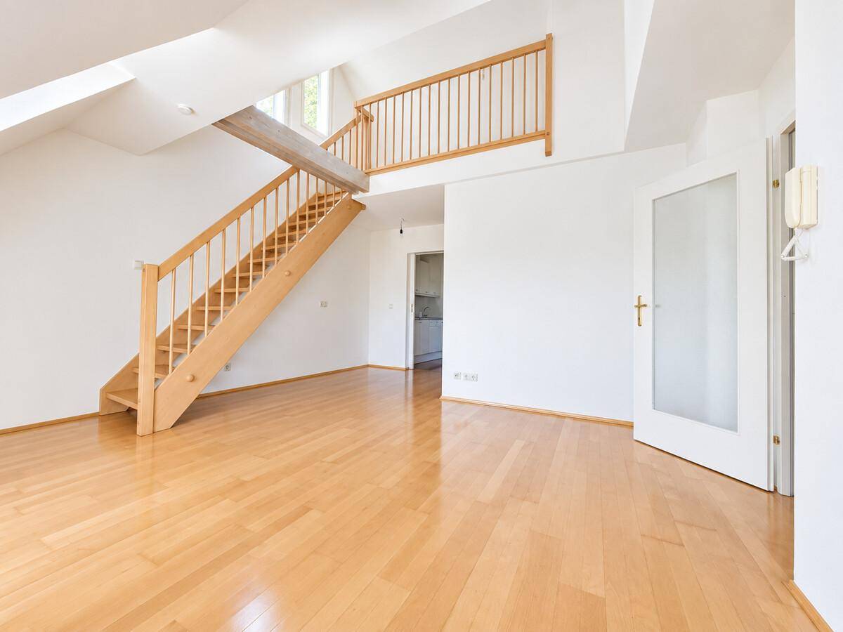 Geräumiges Wohnzimmer mit offener Holztreppe und Zugang zu einer Galerie.
