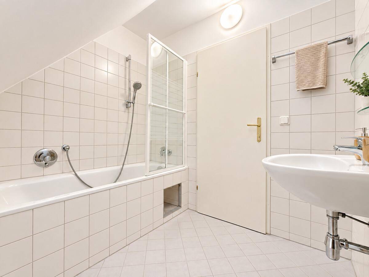 Badezimmer mit Badewanne, Duschabtrennung, Waschbecken und hellen Fliesen.