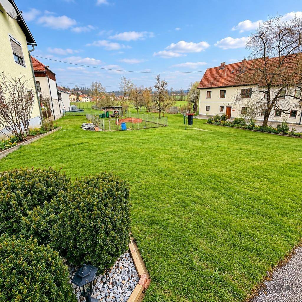 Gepflegter Gartenbereich mit großer Rasenfläche, Hecken und einem kleinen Sportplatz im Hintergrund.