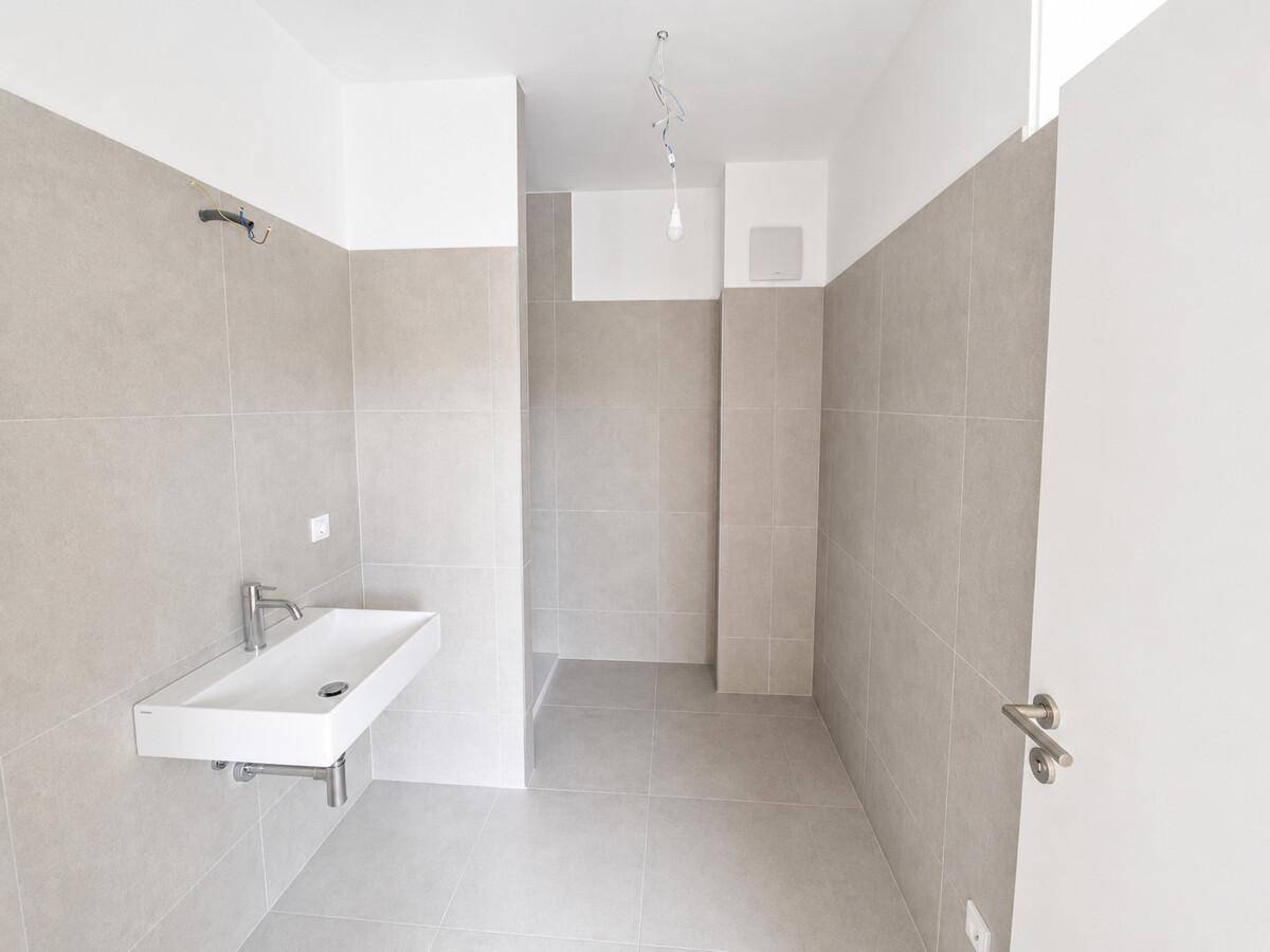 Modernes Badezimmer mit großformatigen grauen Fliesen und wandhängendem Waschbecken.