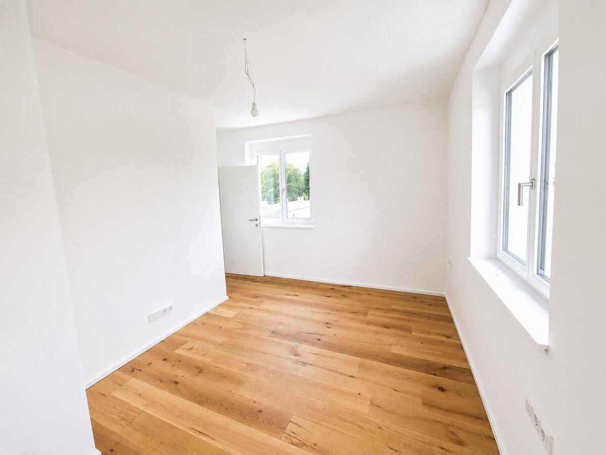 Leeres Schlafzimmer mit hellem Holzparkettboden und großen Fenstern für viel Tageslicht.