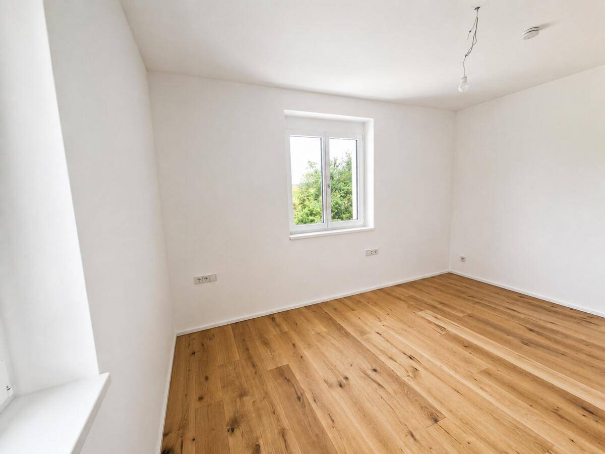 Unmöbliertes Zimmer mit Eichenparkett und Blick ins Grüne durch das Fenster.