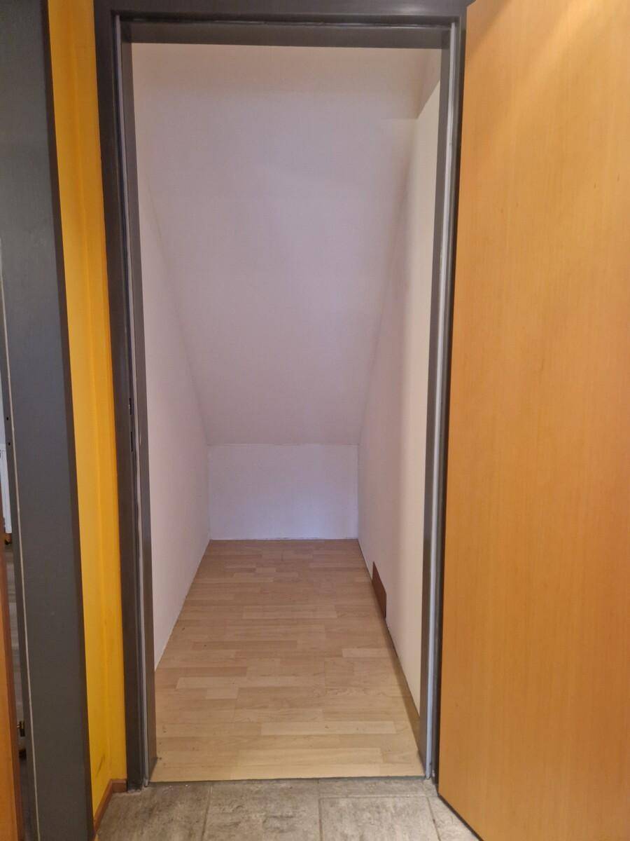 Schmaler, leerer Raum im Dachgeschoss mit schrägen Wänden und hellem Holzfußboden.