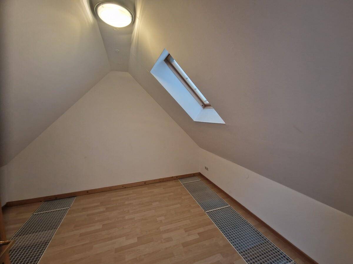Helles Dachgeschosszimmer mit schrägen Wänden, einem Dachfenster und hellem Holzfußboden.