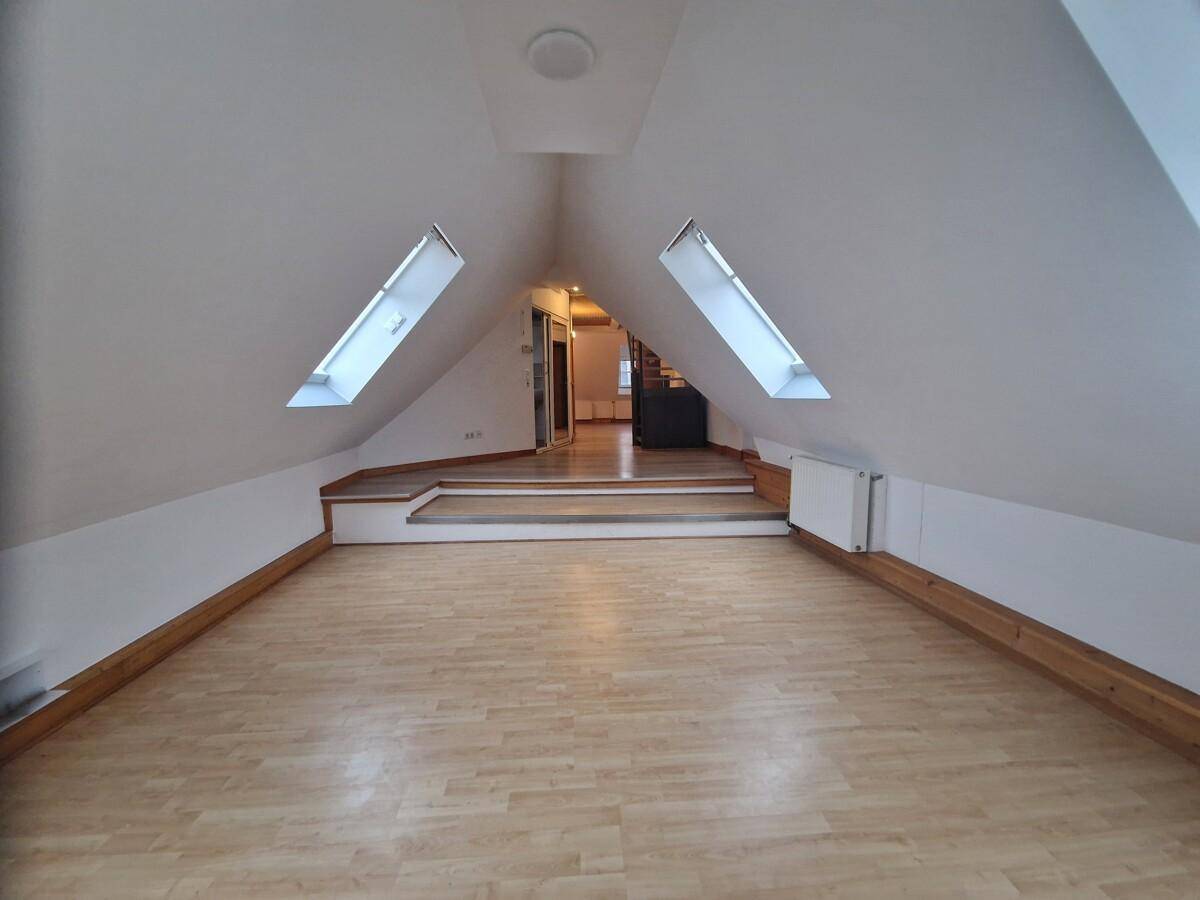 Großzügiger Dachbodenraum mit mehreren Dachfenstern und einer erhöhten Plattform, die zu einem weiteren Bereich führt.