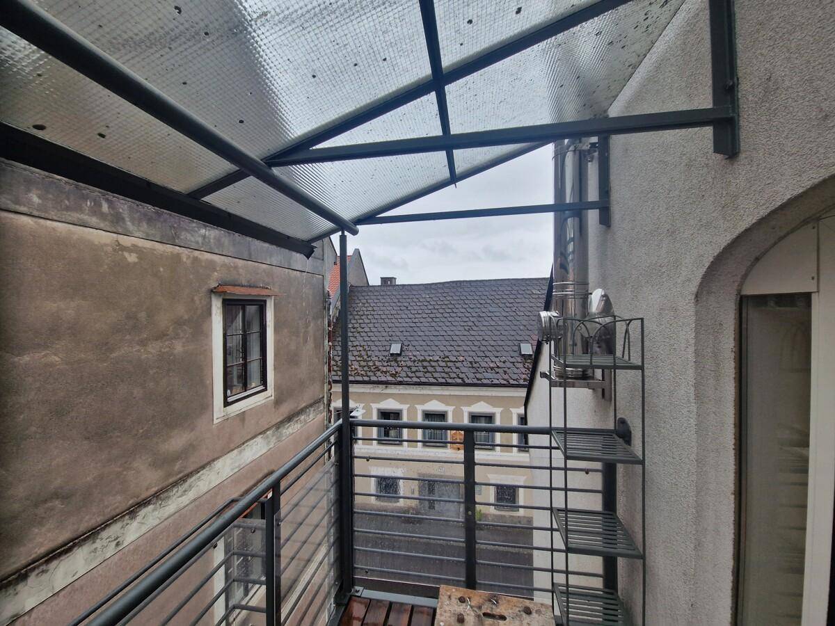 Kleiner überdachter Balkon mit Metallgeländer und Blick auf die umliegenden historischen Gebäude.