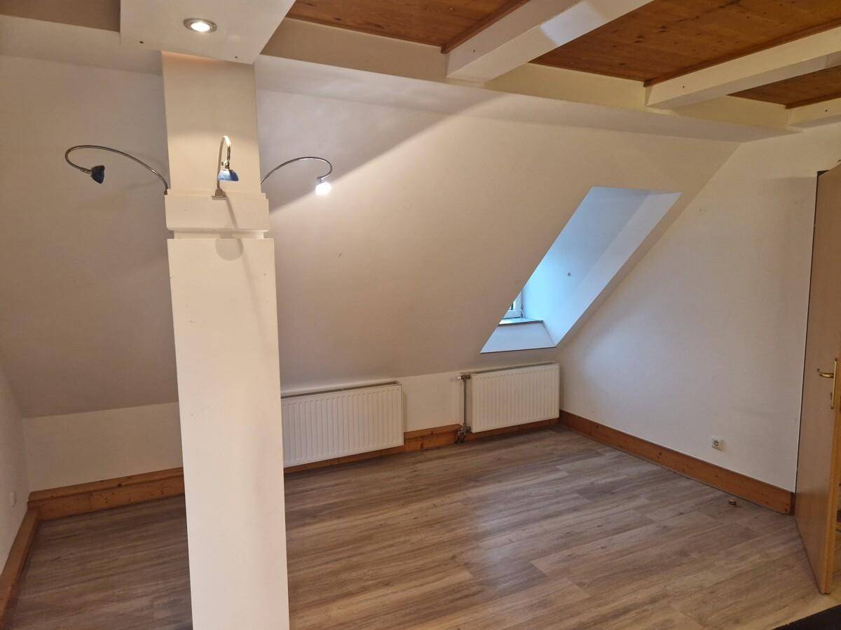 Geräumiges Dachzimmer mit schrägen Wänden, Holzbalken und einem Dachfenster für natürliches Licht.