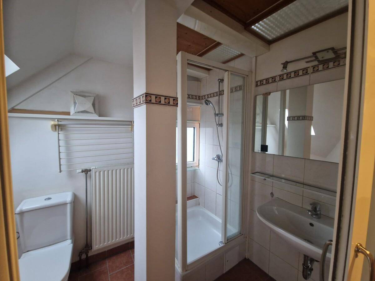 Funktionales Badezimmer im Dachgeschoss mit Duschkabine, WC, Waschbecken und Fliesen an Wänden und Boden.