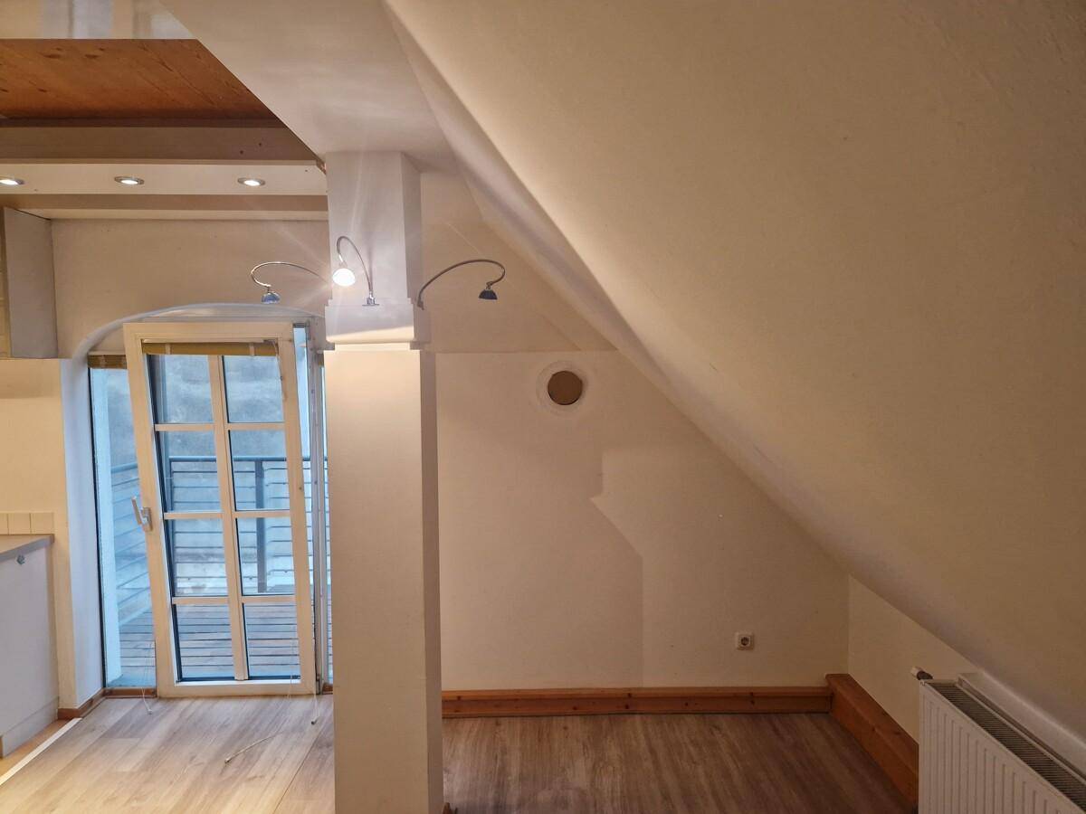 Heller Wohnbereich im Dachgeschoss mit Holzbalken, schrägen Wänden und Zugang zu einem Balkon.