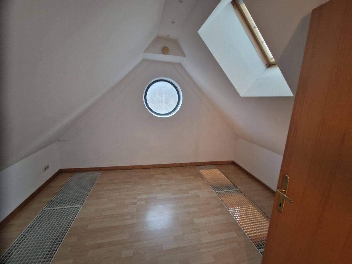 Dachgeschosszimmer mit einzigartigem Rundfenster, Dachfenster und hellem Holzfußboden, bietet viel Potenzial.
