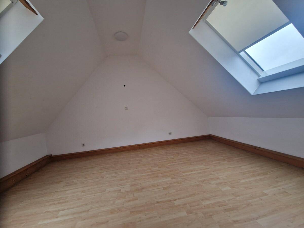 Helles Dachgeschosszimmer mit zwei Dachfenstern und schrägen Wänden, ideal als Schlaf- oder Arbeitsbereich.