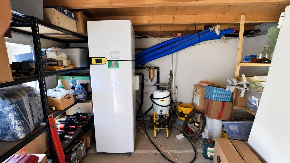 Technikraum mit Wärmepumpe und Lagerregalen, umgeben von verschiedenen Geräten.