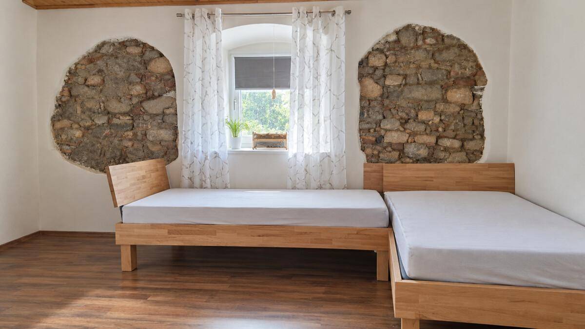 Helles Schlafzimmer mit zwei Holzbetten, Holzboden und dekorativen Steinakzenten an den Wänden.