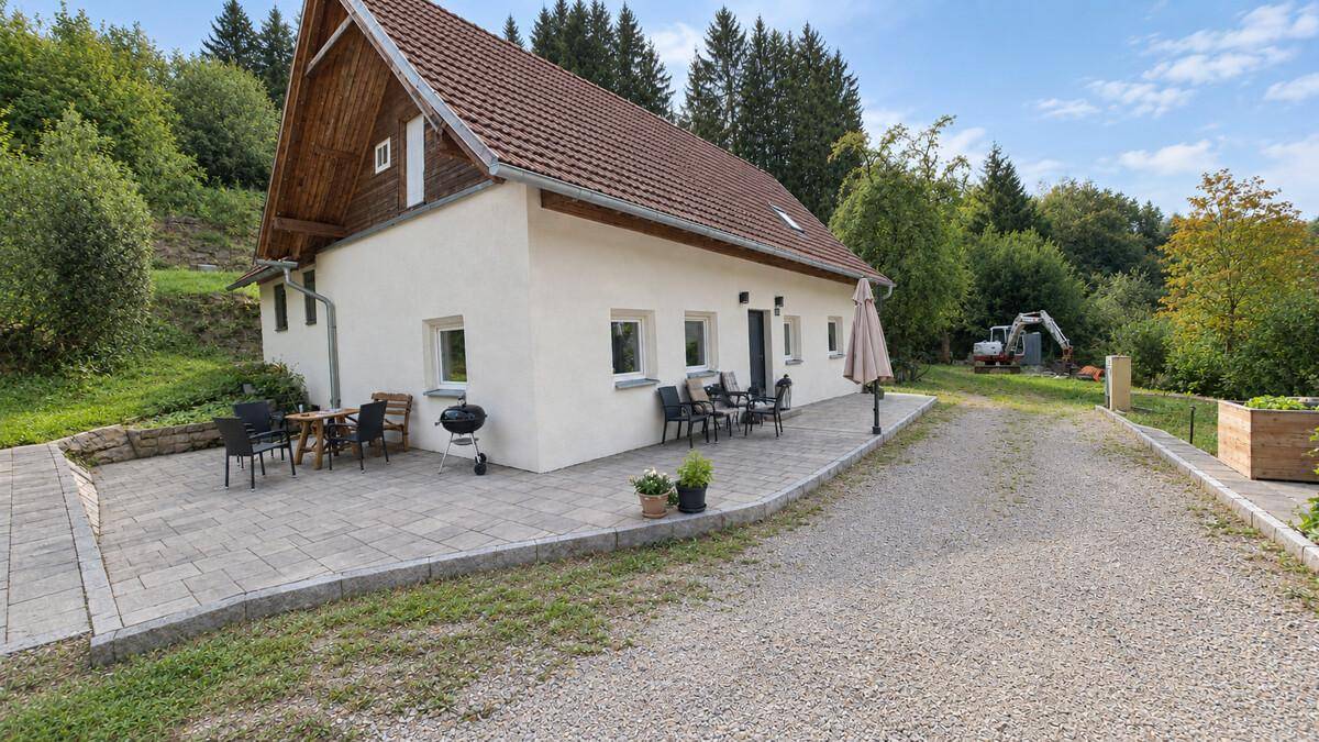 Gemütliche Terrasse am Haus mit Sitzgelegenheiten und Grill, umgeben von Bäumen und Natur.