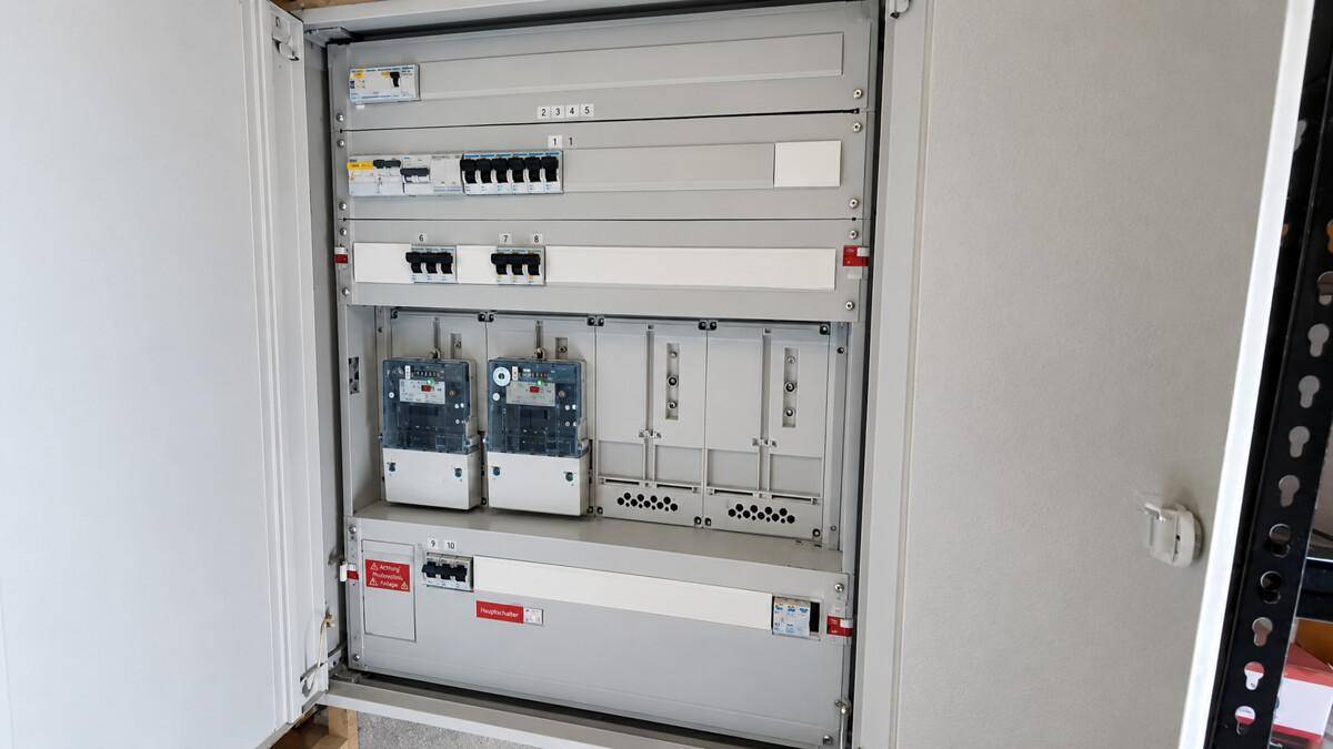 Offener Sicherungskasten mit mehreren Stromzählern und Schaltern in einem Technikraum.