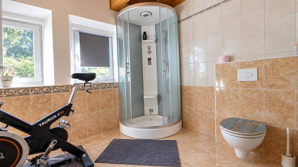 Badezimmer mit beigefarbenen Fliesen, Duschkabine und einem Heimtrainer.