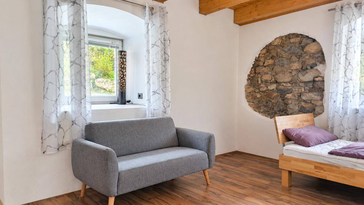 Schlafzimmer mit Holzboden, freigelegten Steinwänden und einem kleinen Sofa am Fenster.