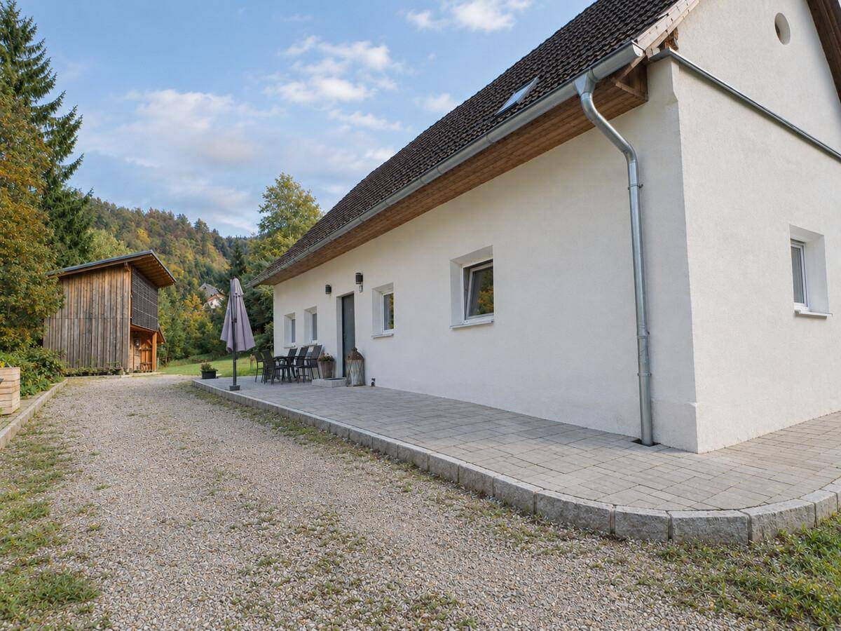 Seitenansicht des Hauses mit gepflasterter Terrasse und angrenzendem Schuppen in ländlicher Umgebung.