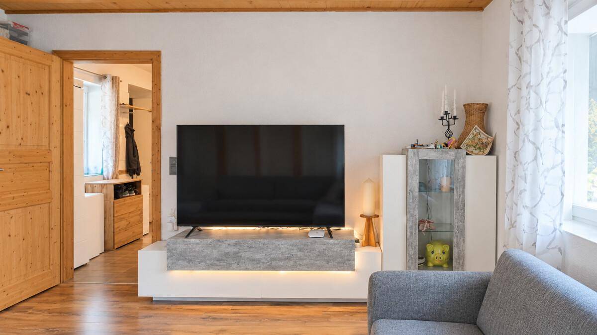 Wohnzimmer mit modernem TV-Möbel, Holzboden und Zugang zu einem weiteren Raum.