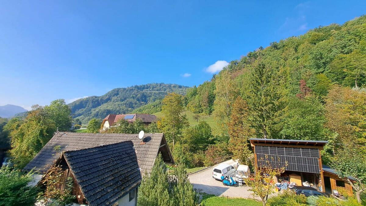Weitläufiger Blick über grüne Hügel und Wälder mit mehreren Häusern in der Ferne.