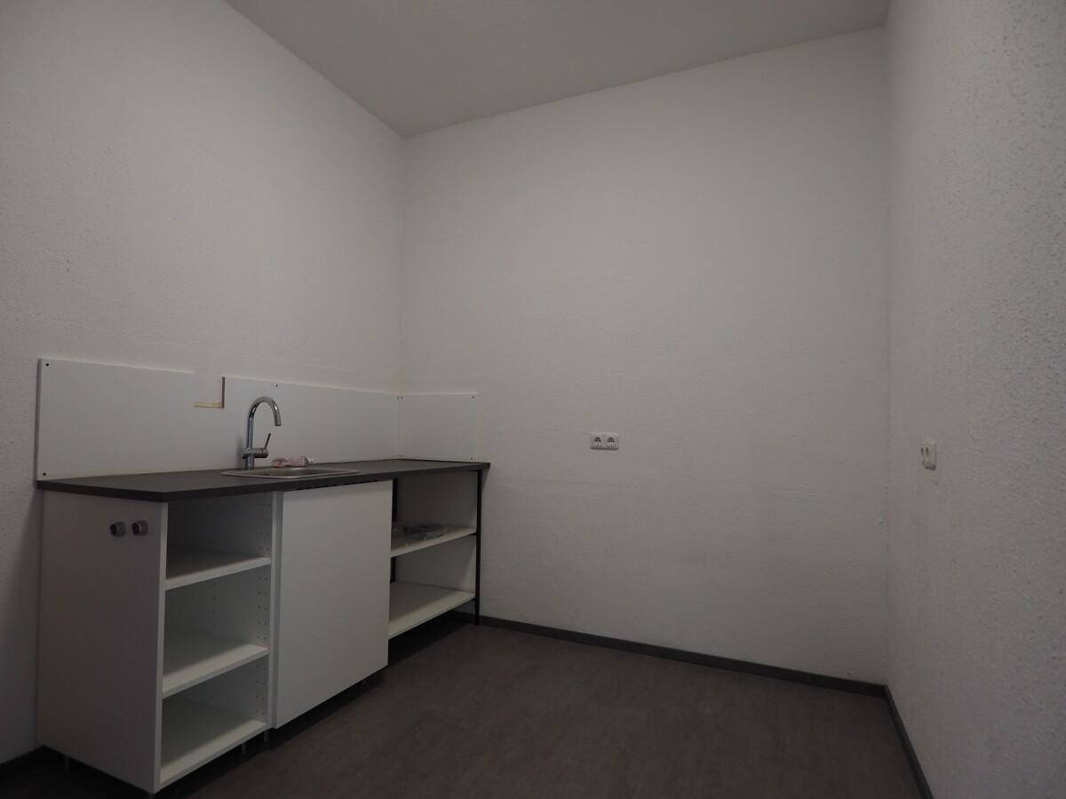 Kleiner Raum mit einfacher Küchenzeile, Spülbecken und offenen Regalen an der Wand für den Gebrauch.