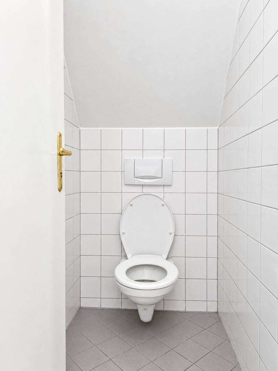 Separates WC mit Wand-WC und weißen Fliesen unter der Dachschräge.
