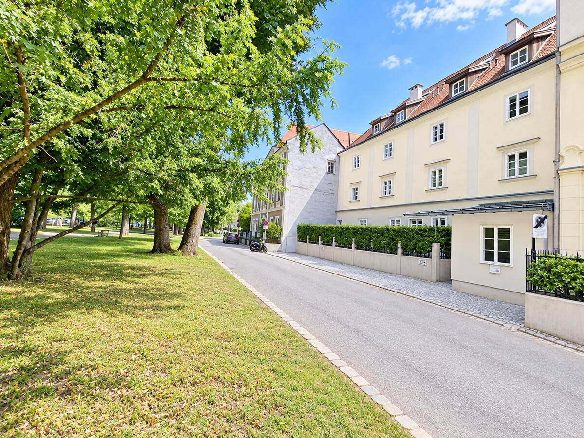 Historisches Gebäude mit gepflegter Fassade, umgeben von Grünflächen und Bäumen.