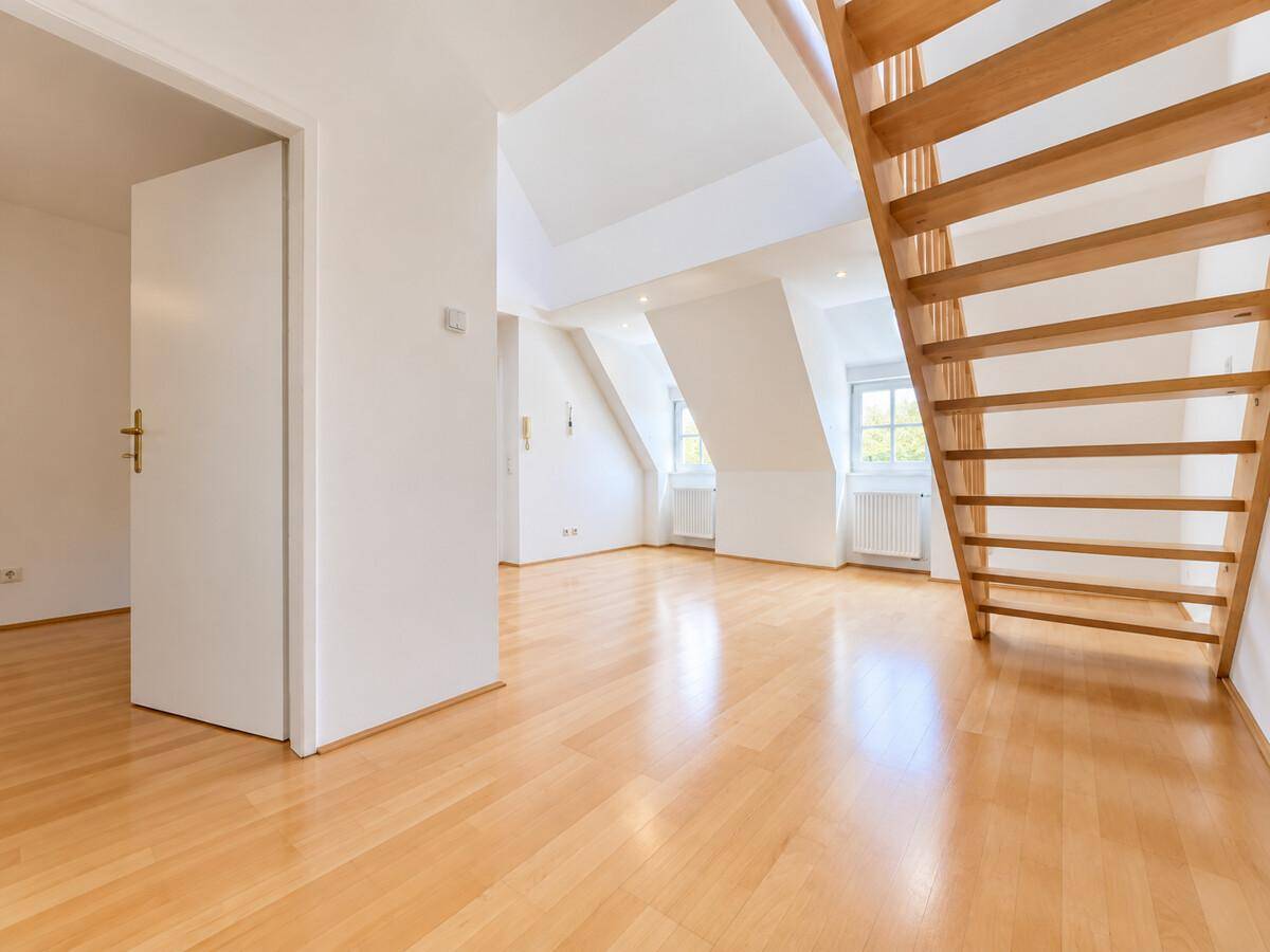 Geräumiges Wohnzimmer mit Parkettboden, Dachschrägen und Blick auf die Fenster.