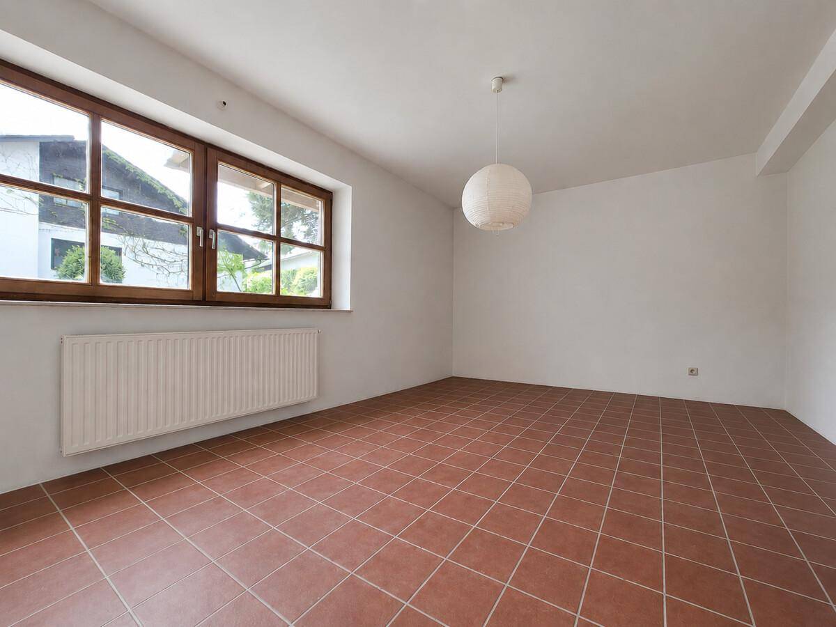 Heller Raum mit großen Holzfenstern und Terrakotta-Fliesenboden, unmöbliert und vielseitig nutzbar.