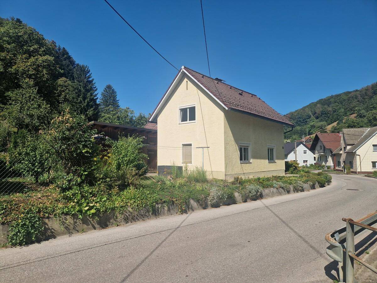 Seitenansicht des Hauses von der Straße aus mit Blick auf die umliegende ländliche Bebauung und Hügel.