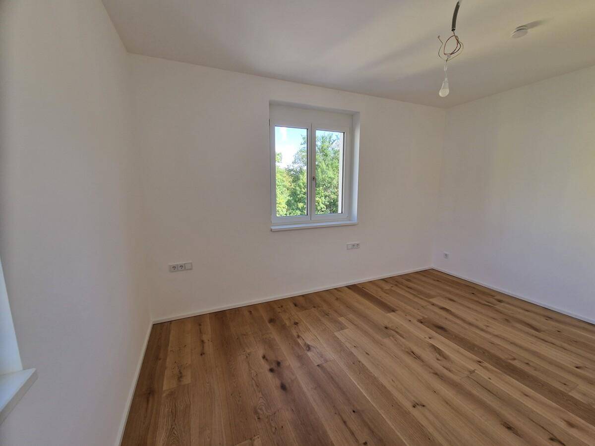 Geräumiges Schlafzimmer mit hellem Holzboden und Blick ins Grüne.