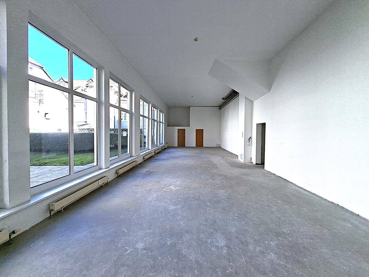 Geräumiger Gewerberaum mit Betonboden und großen Fenstern, die viel Tageslicht hereinlassen.