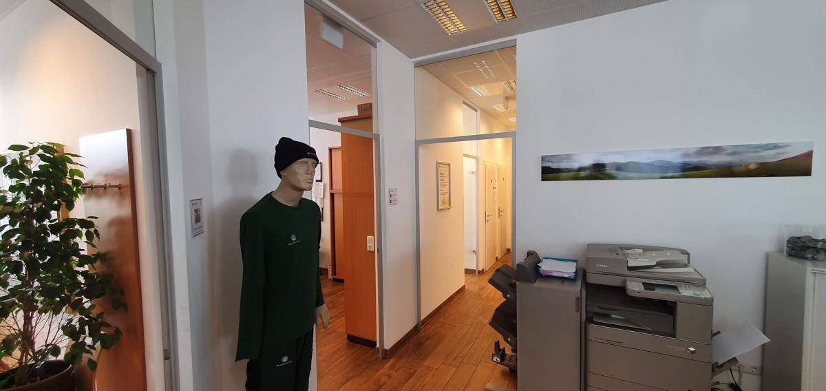 Flur und Bürobereich mit Holzboden, einem Drucker und einer Schaufensterpuppe als Dekorationselement.