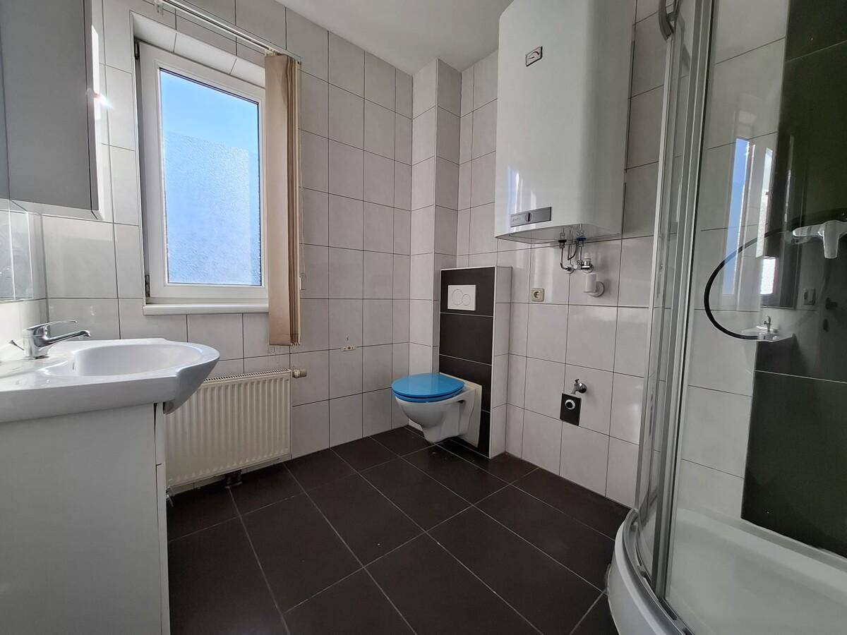Modernes Badezimmer mit Dusche, WC und Waschbecken, gefliest in Weiß und Dunkelgrau.