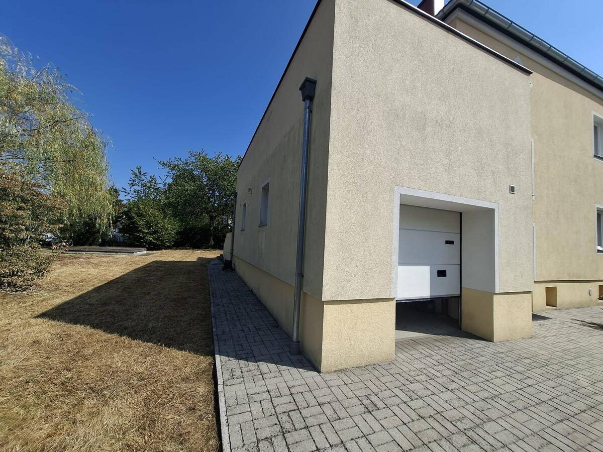Seitenansicht des Hauses mit Garageneinfahrt und gepflastertem Zugang unter blauem Himmel.