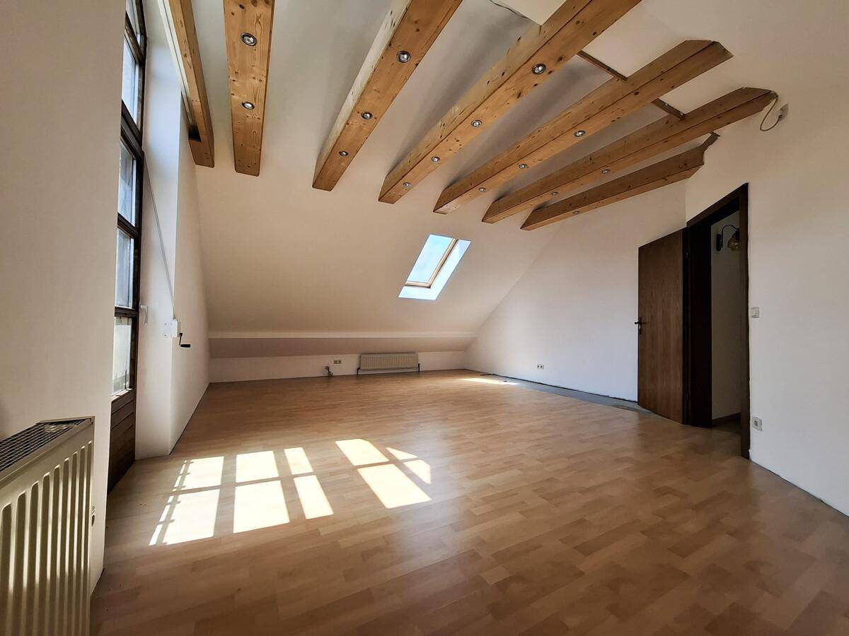 Heller Dachraum mit sichtbaren Holzbalken, Dachfenster und Parkettboden, der viel Potenzial bietet.