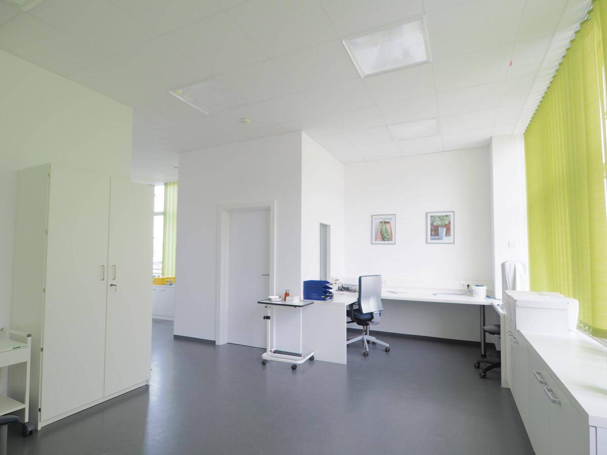 Geräumiges Büro mit Schreibtisch, Stühlen und einem großen Fenster mit grünen Jalousien.
