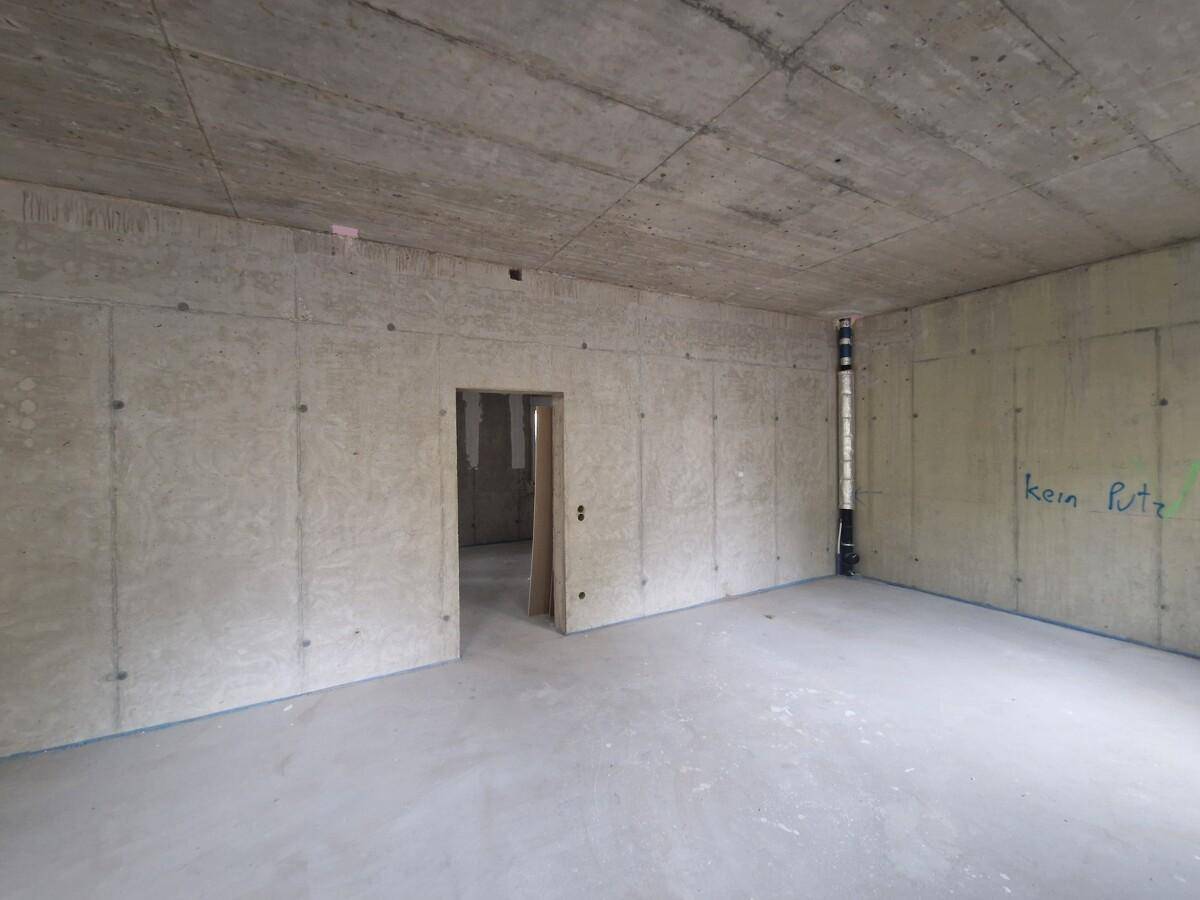 Unfertiger Raum mit Betonwänden, einer Türöffnung und sichtbaren Leitungen.