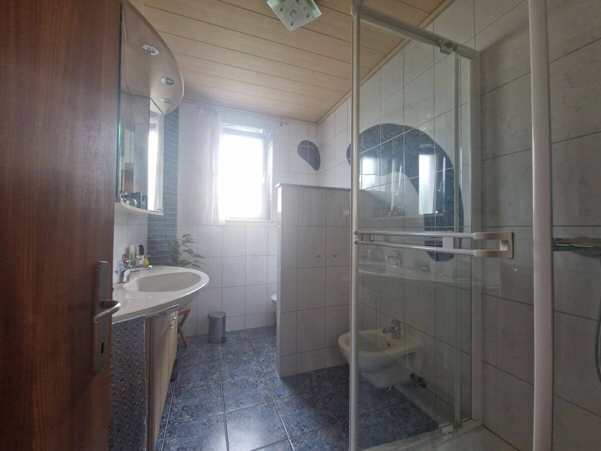 Helles Badezimmer mit Dusche, Bidet, Waschbecken und Fenster, ausgestattet mit blauen Bodenfliesen.