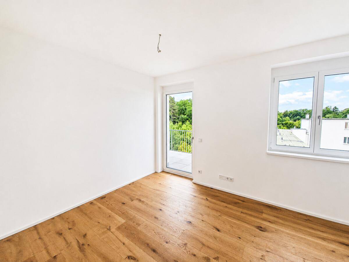 Leeres Zimmer mit Eichenparkett, Zugang zum Balkon und Blick ins Grüne.