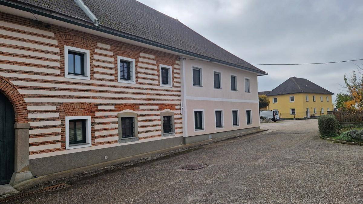 Historisches Gebäude mit Ziegel- und Putzfassade an einer ländlichen Straße unter bewölktem Himmel.